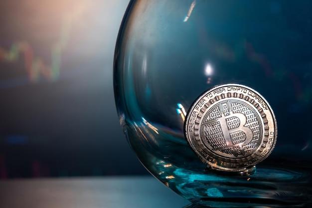 Free photo closeup of a silver bitcoin on a blue reflective surface in a glass and the histogram of currency