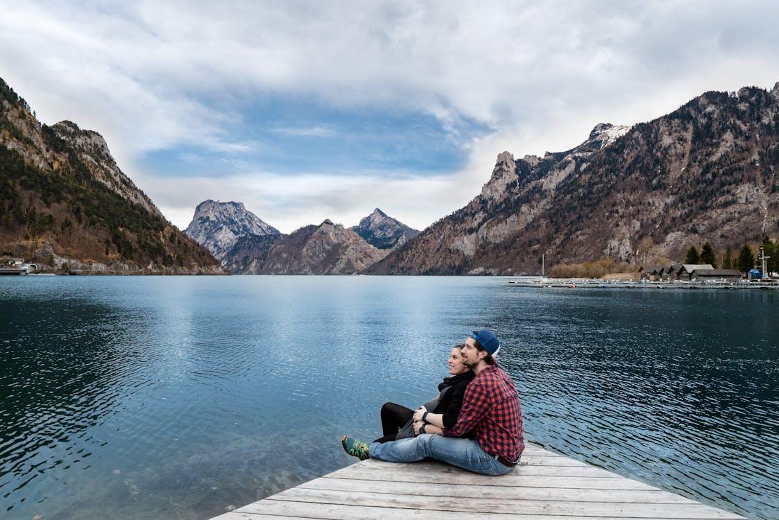 Free Man and Woman Sitting on Brown Wooden Dock Stock Photo